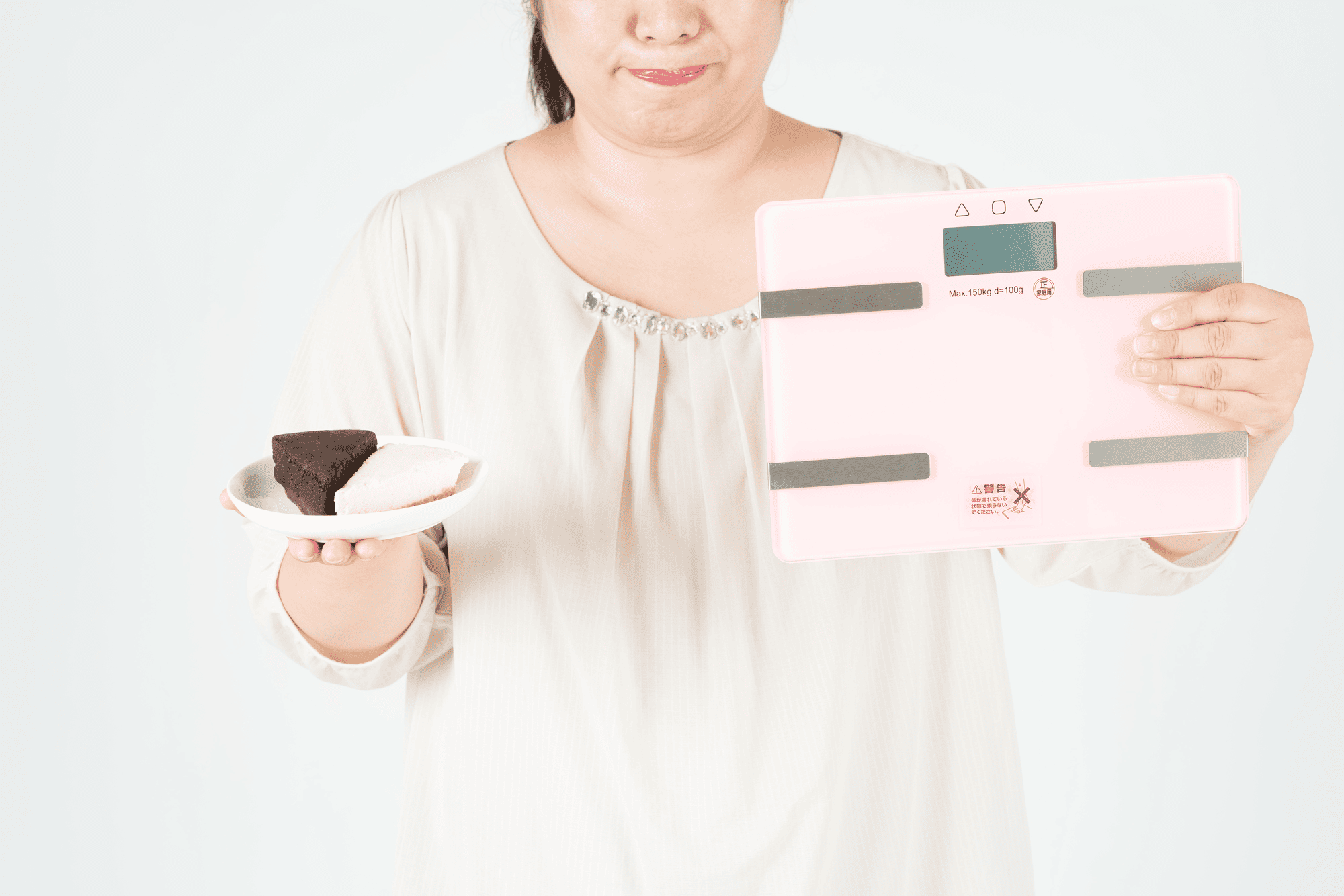 太った理由は必ず日常生活の習慣の中にあります。ケーキと体重計を持つ女性のイメージ写真