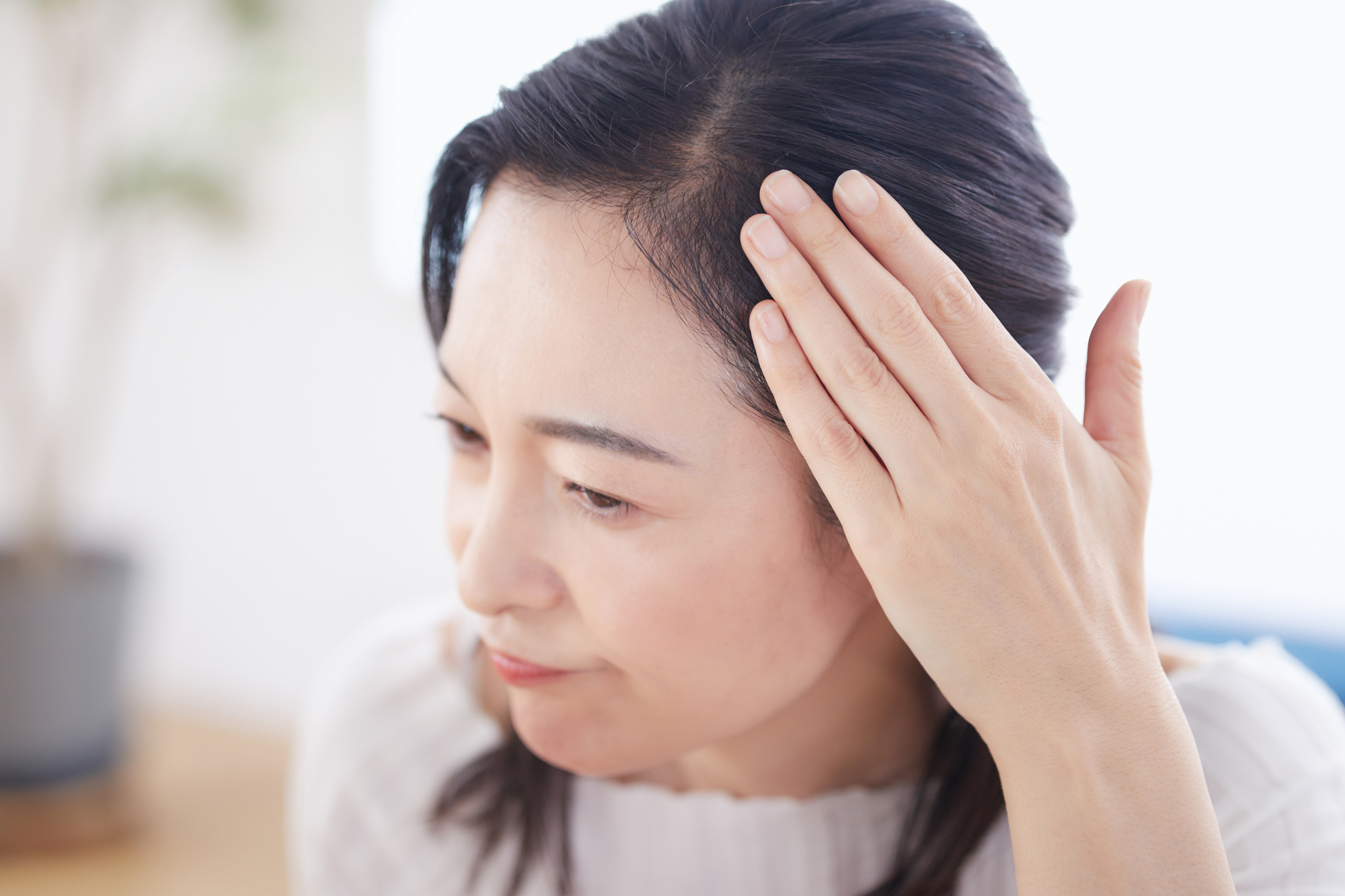 分け目が薄くなる原因には壮年性脱毛症がある。分け目を気にする女性。